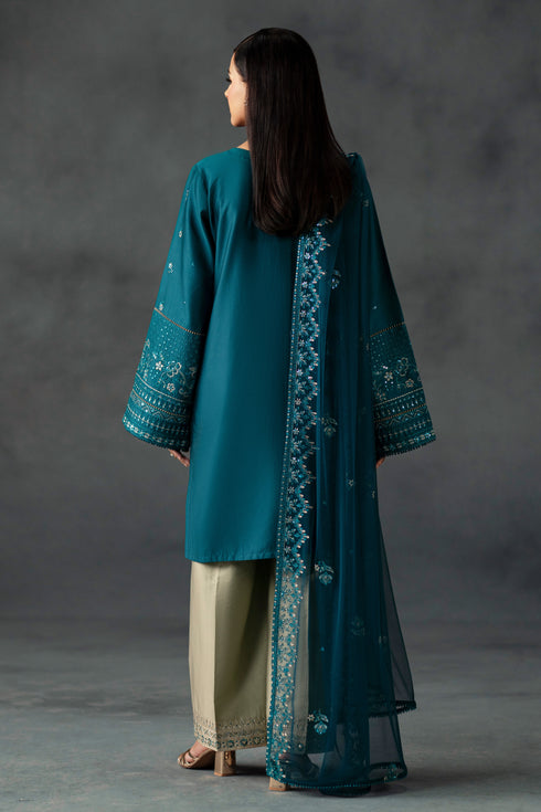 Woman wearing a teal embroidered outfit against a gray background